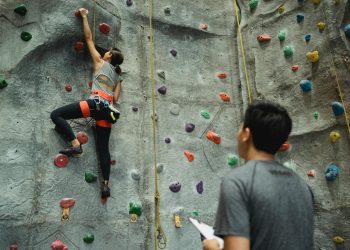 Back view of young female climbing wall while man writing results and watching