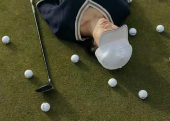 Asian woman in white cap lying on golf course with golf balls and club.