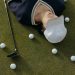 Asian woman in white cap lying on golf course with golf balls and club.